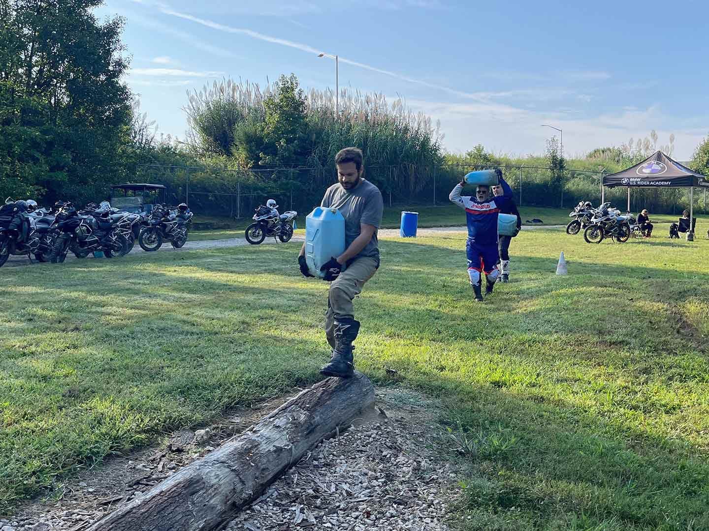 The author carries a full water jug across a log as part of a physical challenge.