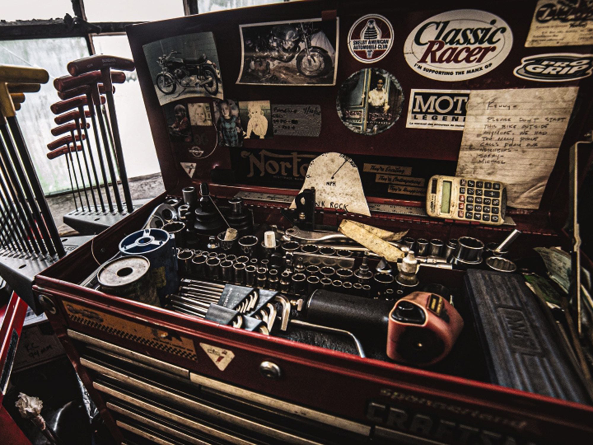 A toolbox lid pasted with family photos, an “I’m supporting the Manx GP” sticker, and one of the band Blonde Redhead.